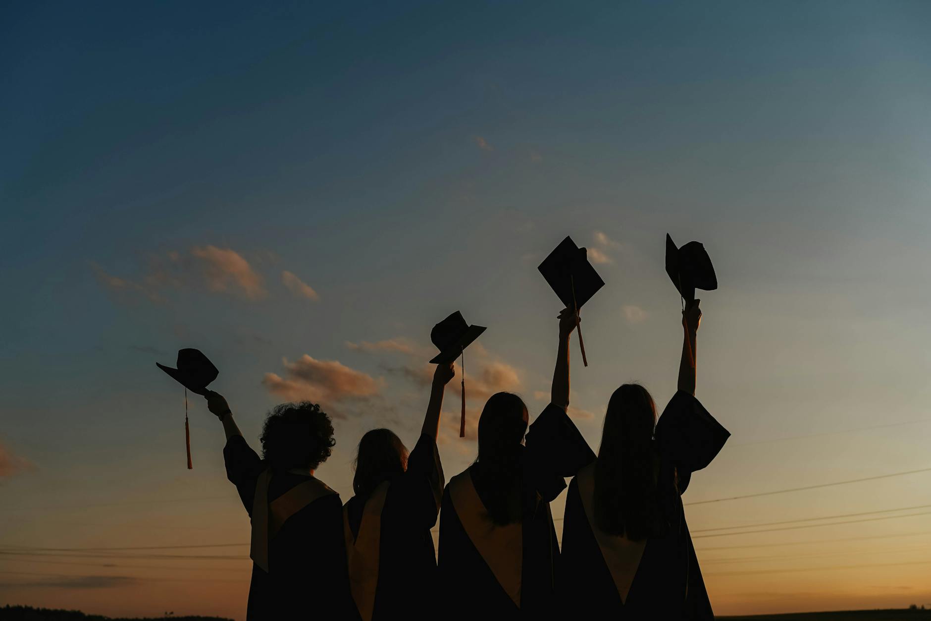 silhouette of people raising their graduation hats