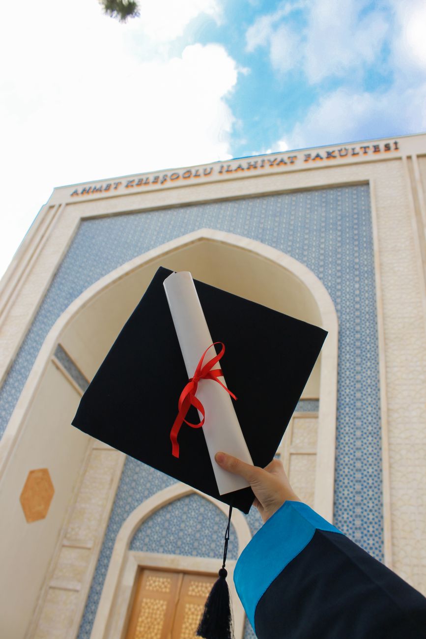 low angle shot of a person holding square academic cap and diploma